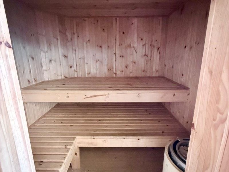 A compact, timber-lined sauna featuring built-in wooden benches and a dedicated sauna heater unit.