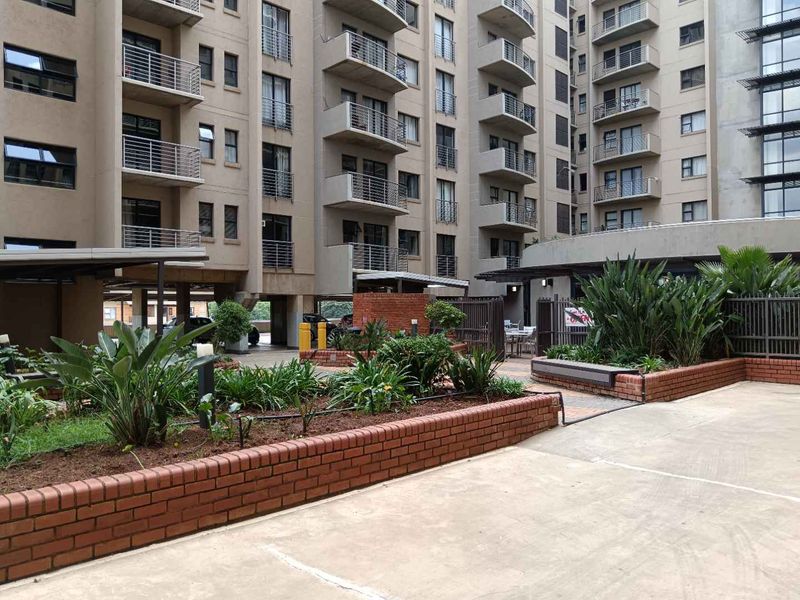 A view of the apartment complex exterior featuring landscaped brick planter boxes, paved common areas, and multi-story residential balconies.