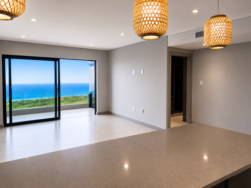 Modern open-plan living area featuring a stone kitchen island, tiled floors, and large sliding doors opening to a balcony with expansive ocean views.