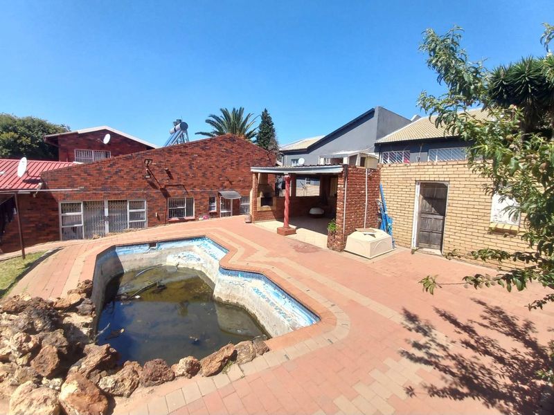 Rear exterior view featuring a paved patio area with a built-in braai and a swimming pool requiring maintenance.