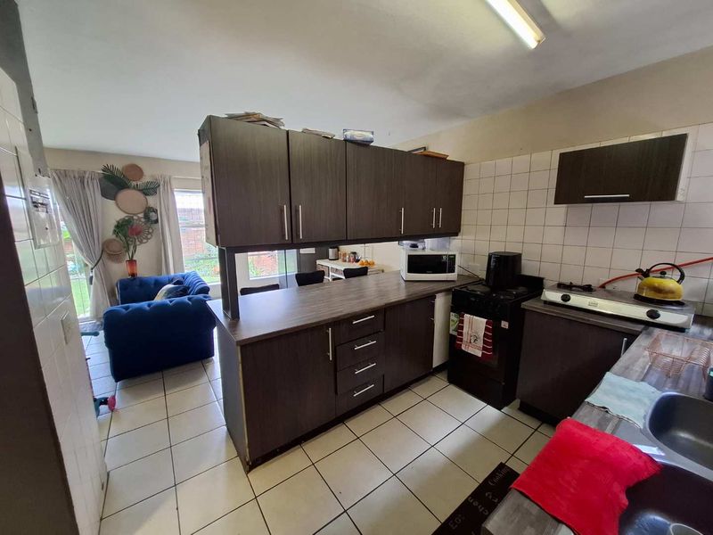 Open plan kitchen featuring dark laminate cabinetry, tiled flooring, and a functional layout connecting to the living area.