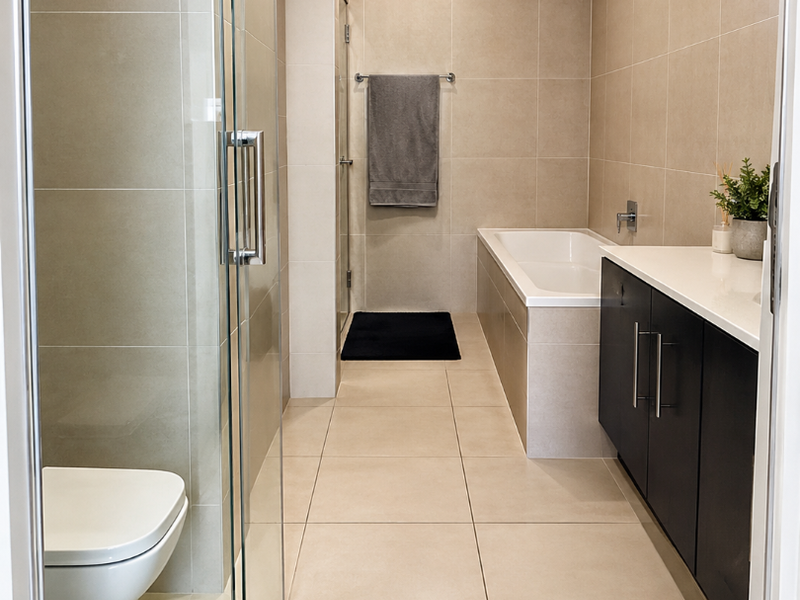 Modern bathroom featuring a glass-enclosed shower, built-in bathtub, wall-mounted toilet, and a sleek vanity cabinet with neutral floor-to-ceiling tiling.