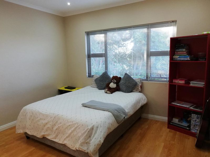 A well-maintained bedroom featuring laminate flooring, recessed downlights, and large windows fitted with venetian blinds.