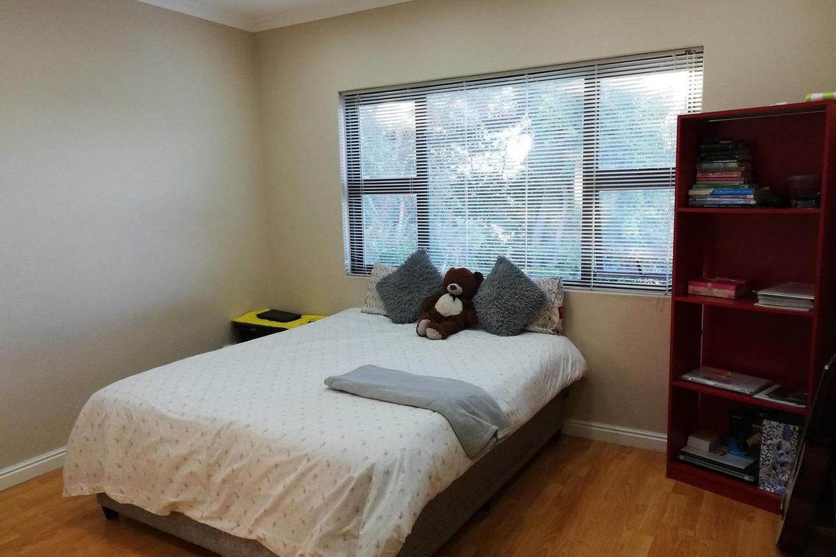 A well-maintained bedroom featuring laminate flooring, recessed downlights, and large windows fitted with venetian blinds.