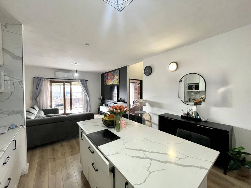 Modern open-plan living area featuring a central kitchen island with stone countertop, integrated hob, and seamless flow to the outdoor patio area.