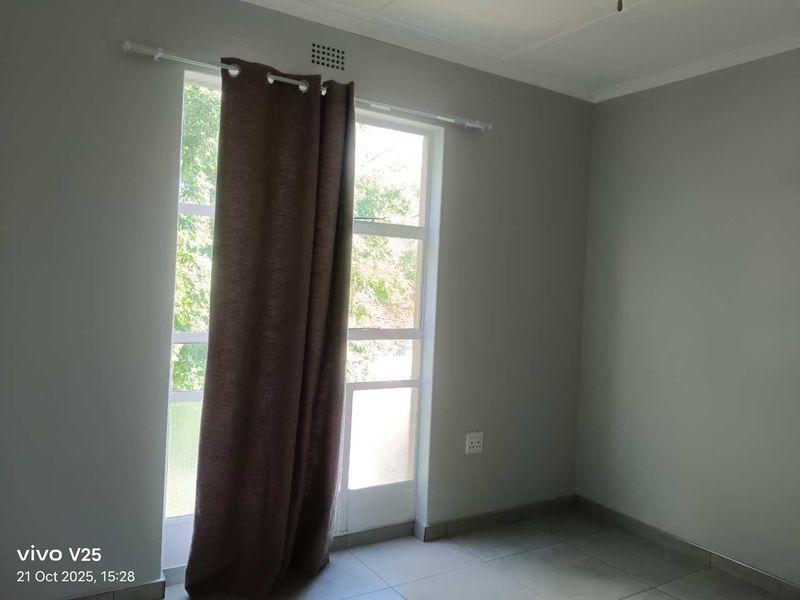 A bright, empty bedroom featuring neutral wall paint, tiled flooring, and a large window providing natural light.