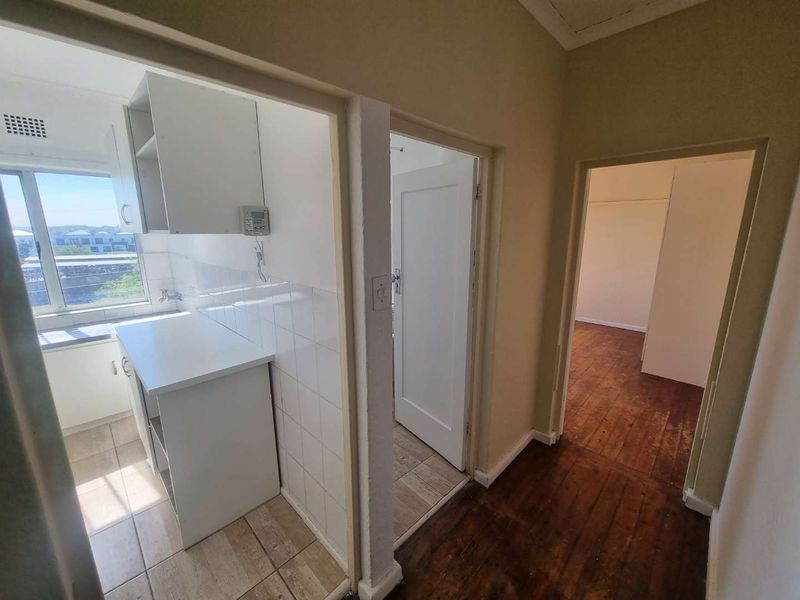 A hallway connecting to a kitchen area and adjacent rooms, featuring a mix of tiled and wooden flooring with dated finishes.