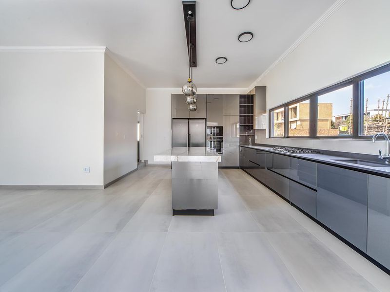 Modern, spacious kitchen featuring high-gloss cabinetry, a central island with stone countertop, integrated appliances, and large windows providing ample natural light.