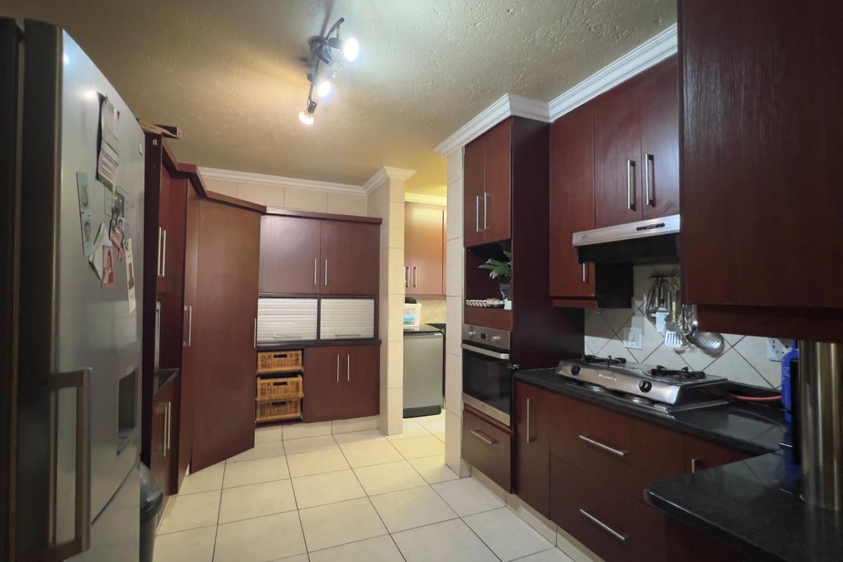 A functional kitchen featuring dark wood cabinetry, granite countertops, a built-in oven, and a gas hob with an extractor fan.
