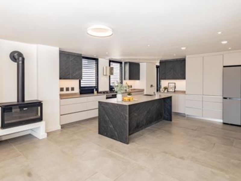 Modern open-plan kitchen featuring a large stone-topped island, sleek cabinetry, integrated appliances, and a contemporary freestanding fireplace in the adjacent living area.