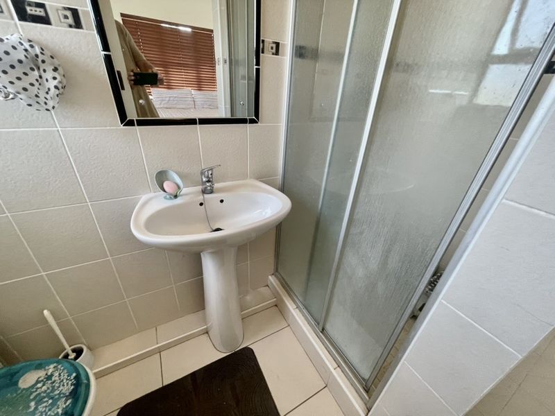 Compact bathroom featuring a pedestal basin, mixer tap, and a glass-enclosed shower with tiled walls and flooring.