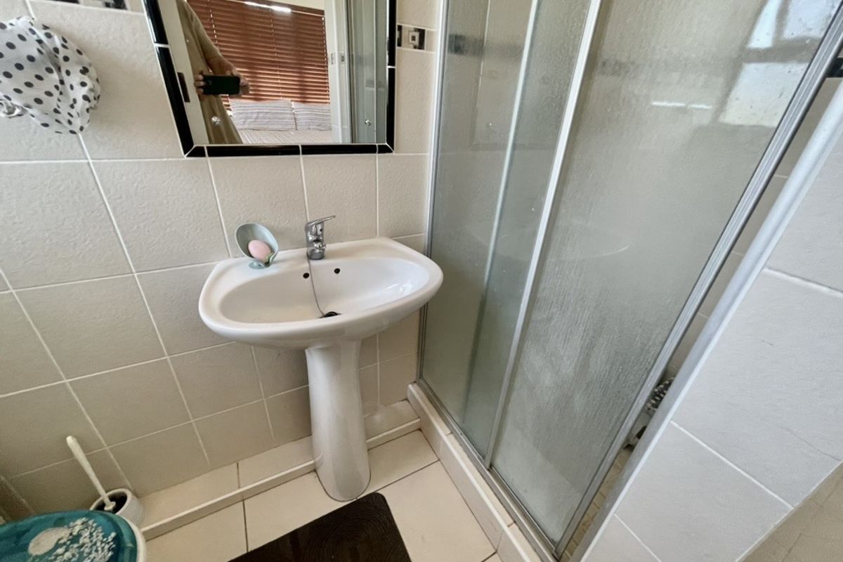 Compact bathroom featuring a pedestal basin, mixer tap, and a glass-enclosed shower with tiled walls and flooring.