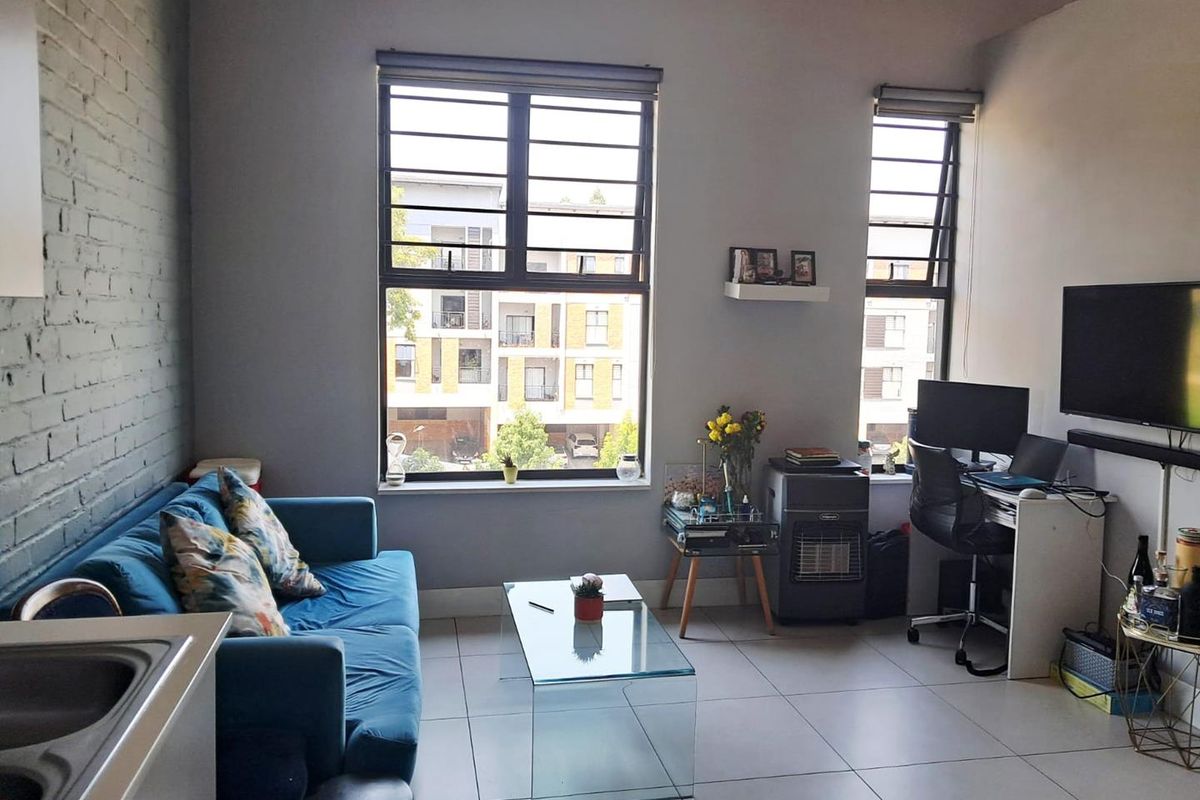 A bright living area featuring large windows with security bars, tiled flooring, and an exposed brick feature wall.