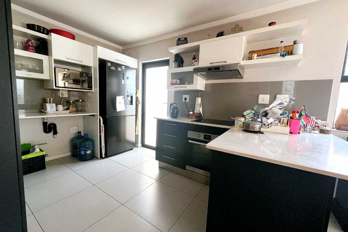 Modern kitchen featuring dark cabinetry, white countertops, built-in oven, extractor fan, and tiled flooring with direct access to the exterior.