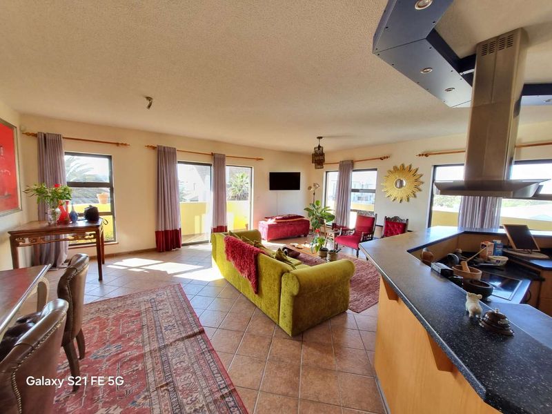 Spacious open-plan living and kitchen area featuring tiled flooring, a central kitchen island with an extractor fan, and large sliding doors leading to a balcony.