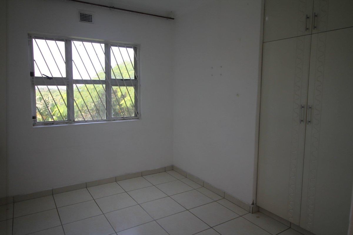 A vacant bedroom featuring tiled flooring, built-in cupboards, and a window fitted with security bars.