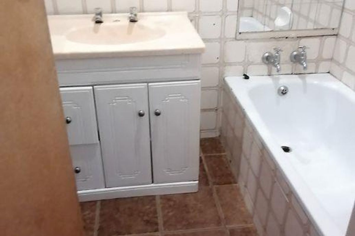 A functional bathroom featuring a vanity cabinet with integrated basin, a standard bathtub, and tiled wall and floor finishes.