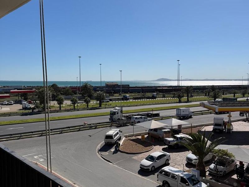 Elevated view from a balcony overlooking a busy road, petrol station, and distant coastal landscape.