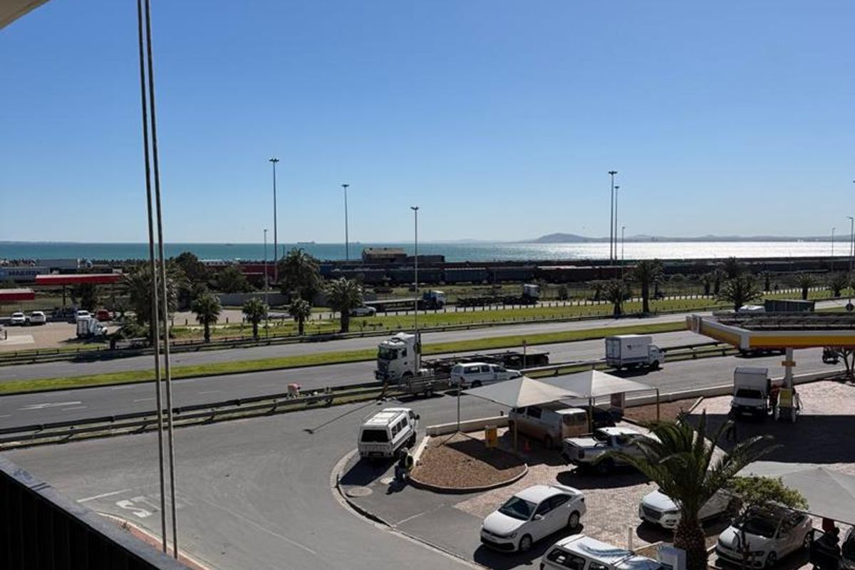 Elevated view from a balcony overlooking a busy road, petrol station, and distant coastal landscape.