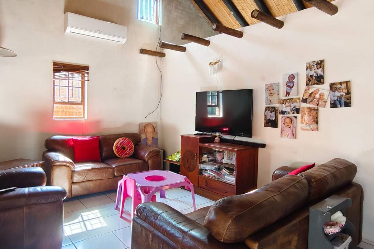 A living room featuring a vaulted ceiling with exposed timber beams, tiled flooring, and a wall-mounted air conditioning unit.