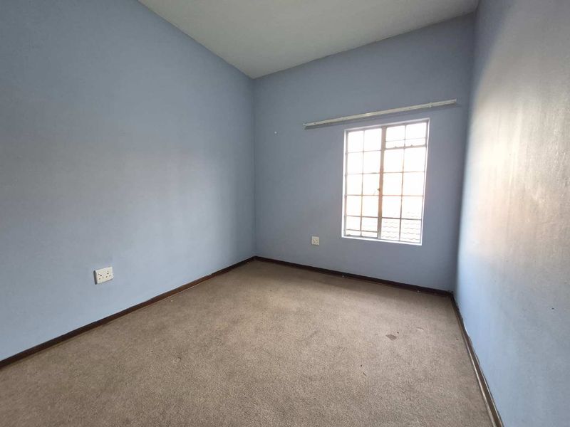 An empty bedroom featuring carpet flooring, blue painted walls, and a window with a curtain rail.