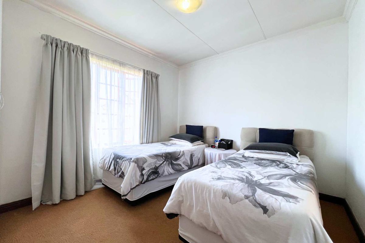 A well-lit bedroom featuring neutral carpeting, crown molding, and large windows with curtain tracks.