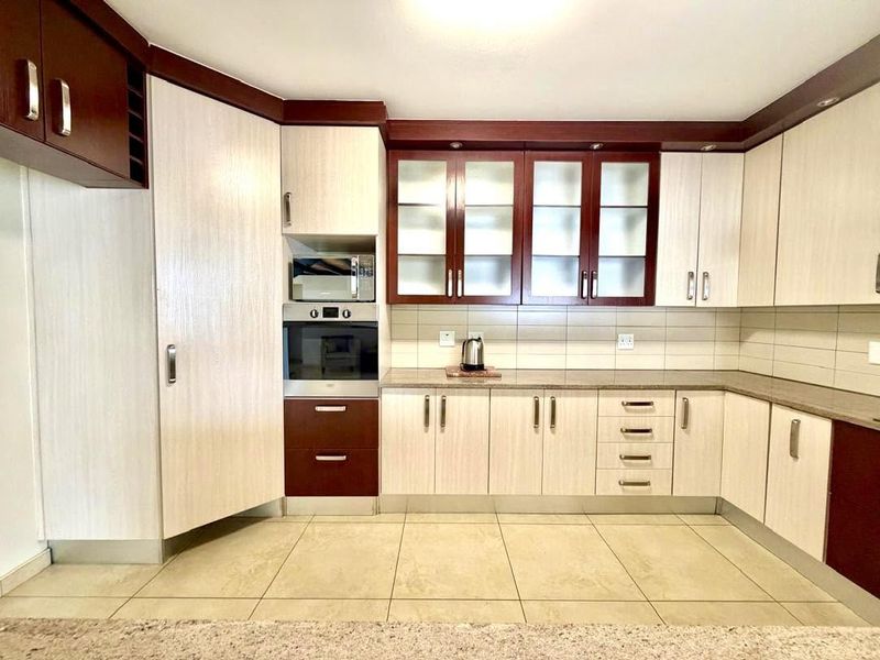 A clean, functional kitchen featuring two-tone cabinetry, built-in oven and microwave, tiled backsplash, and neutral floor tiles.