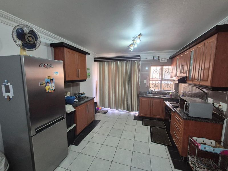 A functional kitchen featuring wood-finish cabinetry, granite countertops, tiled flooring, and a window with security bars, providing a practical workspace.
