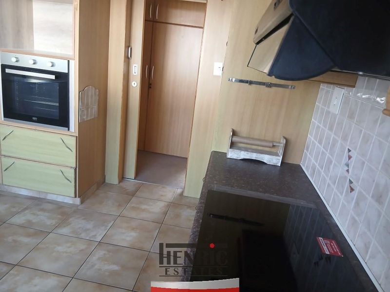 A functional kitchen featuring built-in oven, extractor fan, ceramic hob, tiled splashback, and laminate cabinetry with tiled flooring.