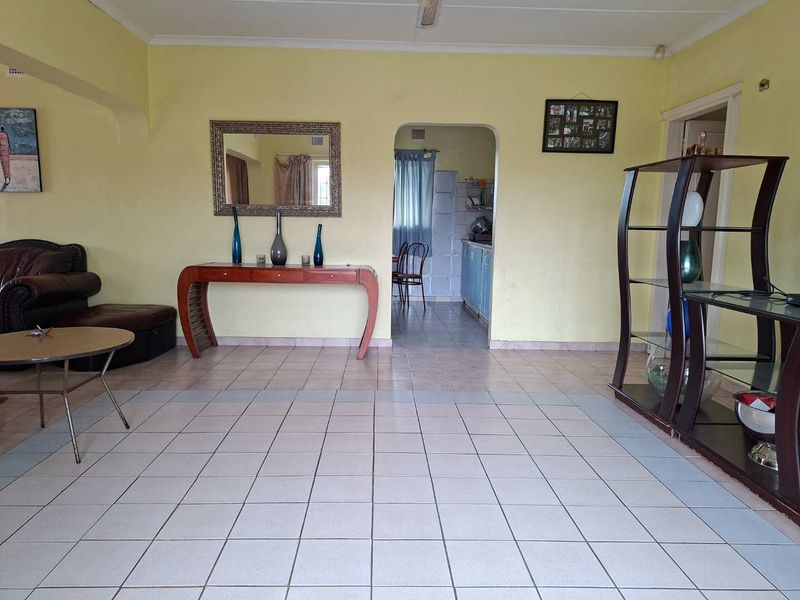 Spacious living area featuring ceramic floor tiles and an arched doorway leading to the kitchen, offering a functional layout with potential for modernization.