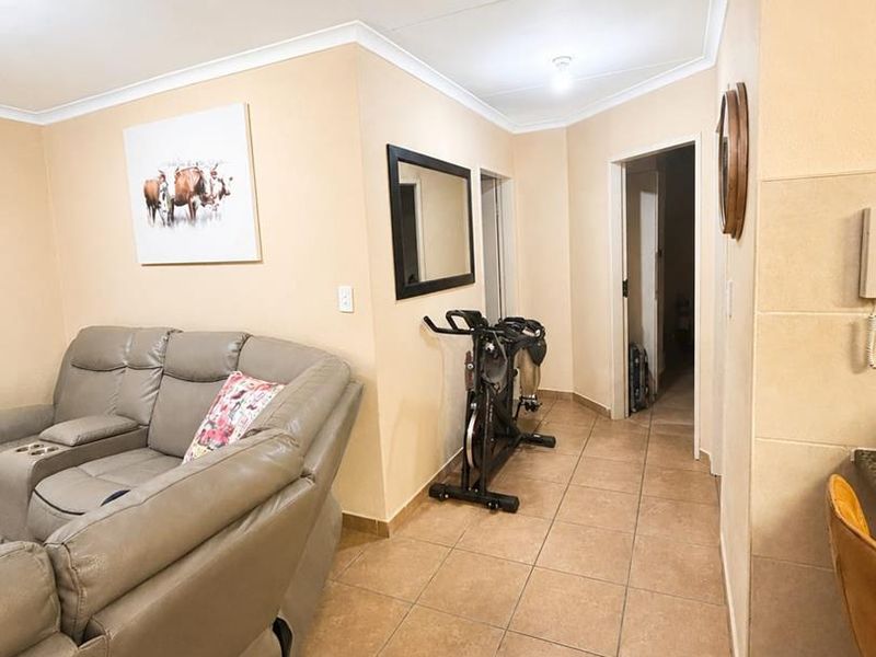 A living area featuring neutral wall tones and tiled flooring, providing a functional space with access to adjacent rooms.