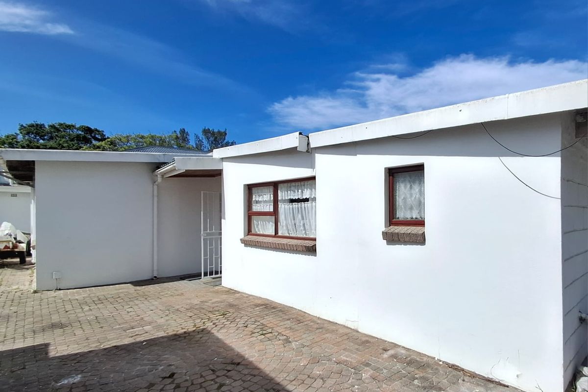 Rear exterior view of the property featuring a paved courtyard area, security gate, and white rendered walls with brick window sills.