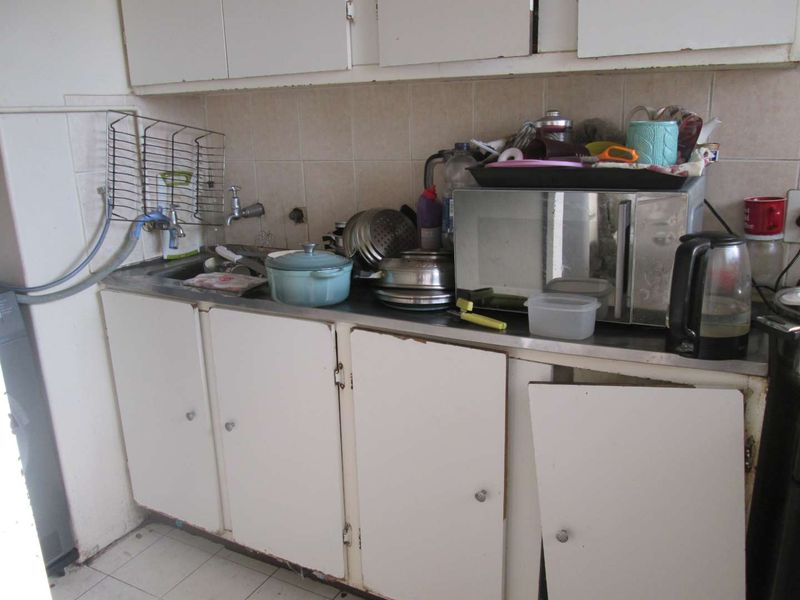 A dated kitchen area featuring built-in cabinetry, a stainless steel sink, and tiled backsplash, currently showing significant wear and tear on the cabinet fixtures.