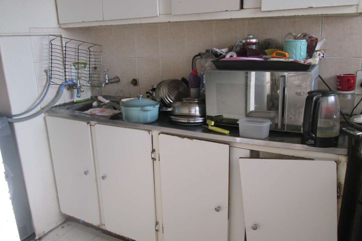 A dated kitchen area featuring built-in cabinetry, a stainless steel sink, and tiled backsplash, currently showing significant wear and tear on the cabinet fixtures.