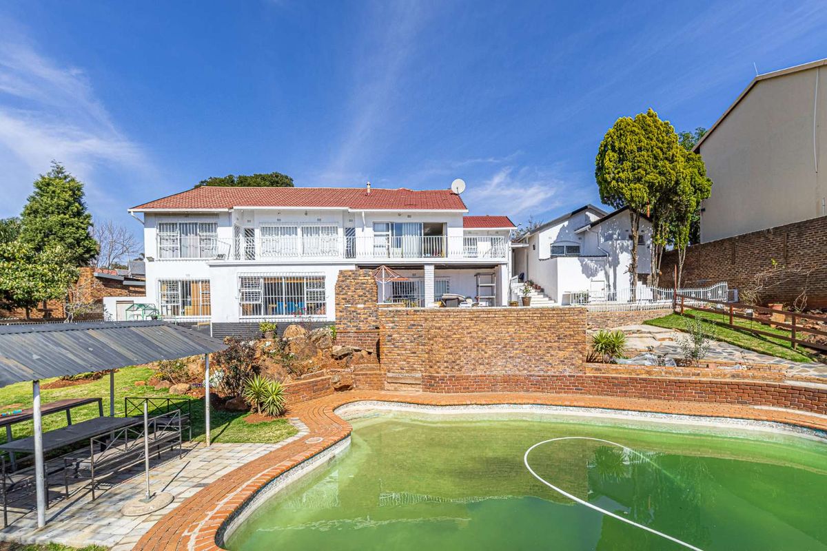 Rear view of a multi-level house featuring a swimming pool, brick retaining walls, a paved patio area, and a covered outdoor structure.