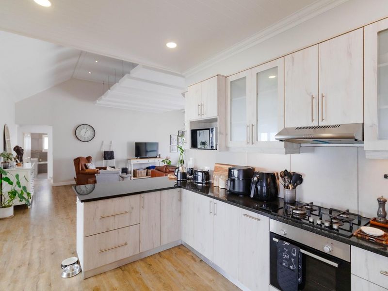 Modern open-plan kitchen featuring light wood-grain cabinetry, granite countertops, and integrated appliances, flowing seamlessly into the adjacent living area.