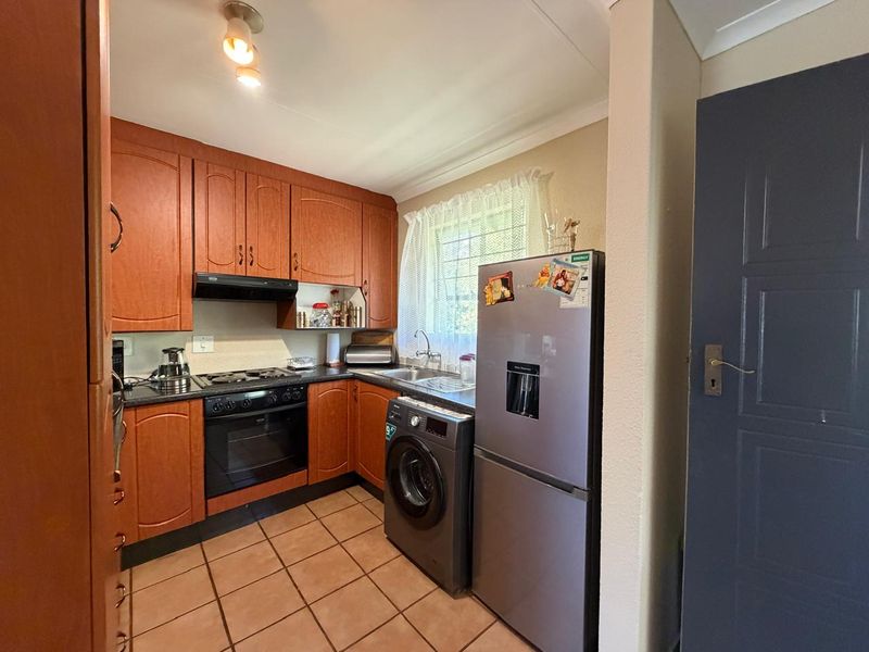 A functional kitchen featuring wood-finish cabinetry, dark countertops, built-in oven and hob, and tiled flooring with a window for natural light.