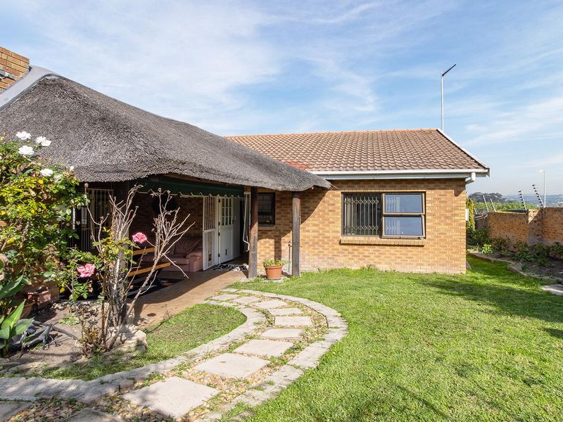 Rear view of a brick house featuring a thatched roof section, a covered patio area, and a landscaped garden with a paved walkway.