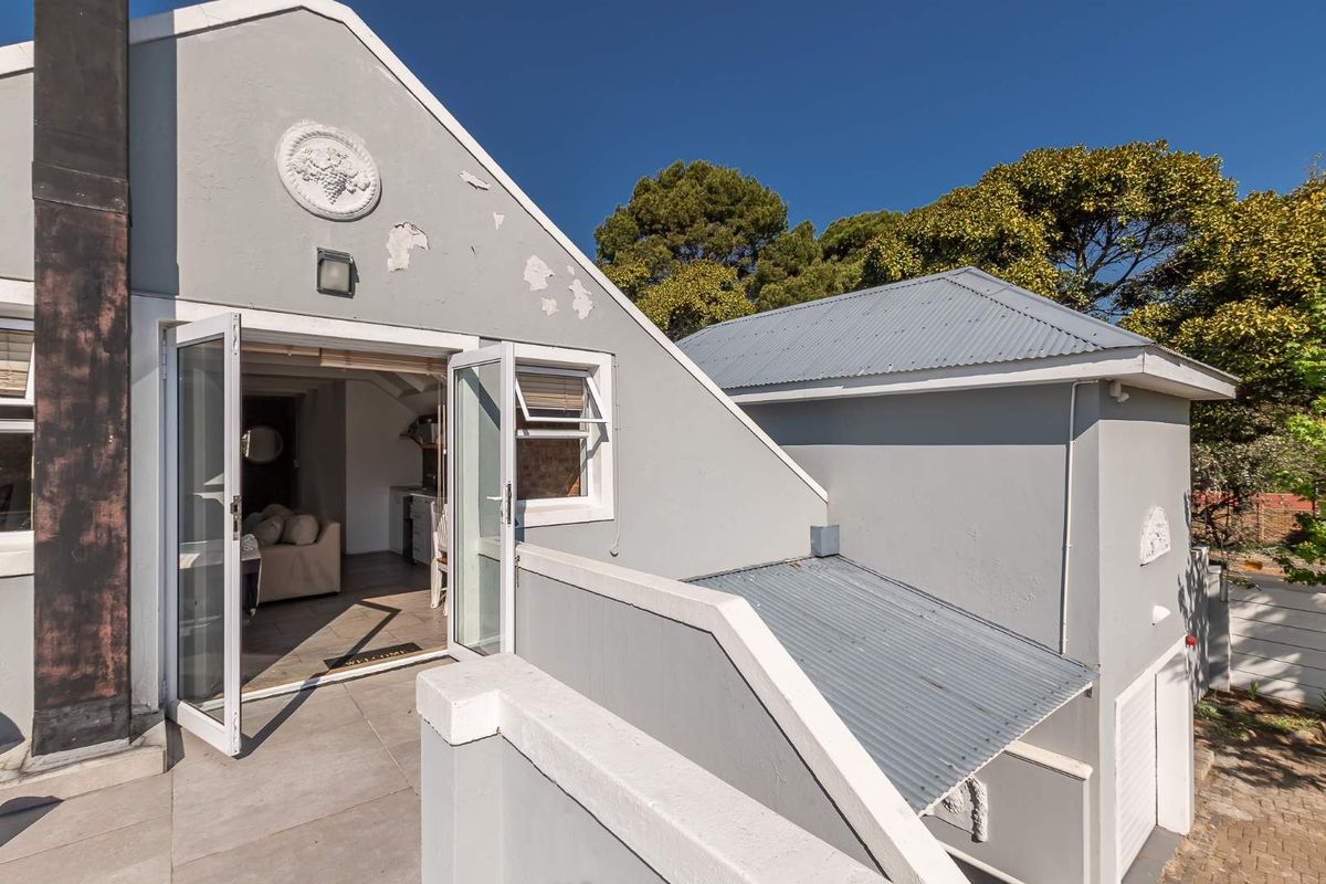 Rear exterior view of the property featuring a tiled patio, french doors, and a corrugated metal roof with visible exterior paint wear.