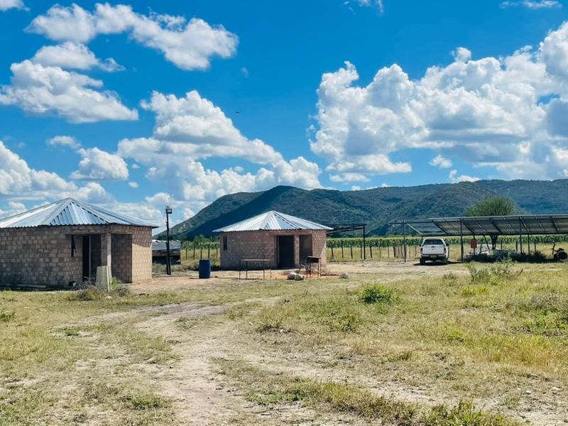 A rural farm property featuring two detached brick structures with metal roofs and a large solar panel installation set against a mountain backdrop.