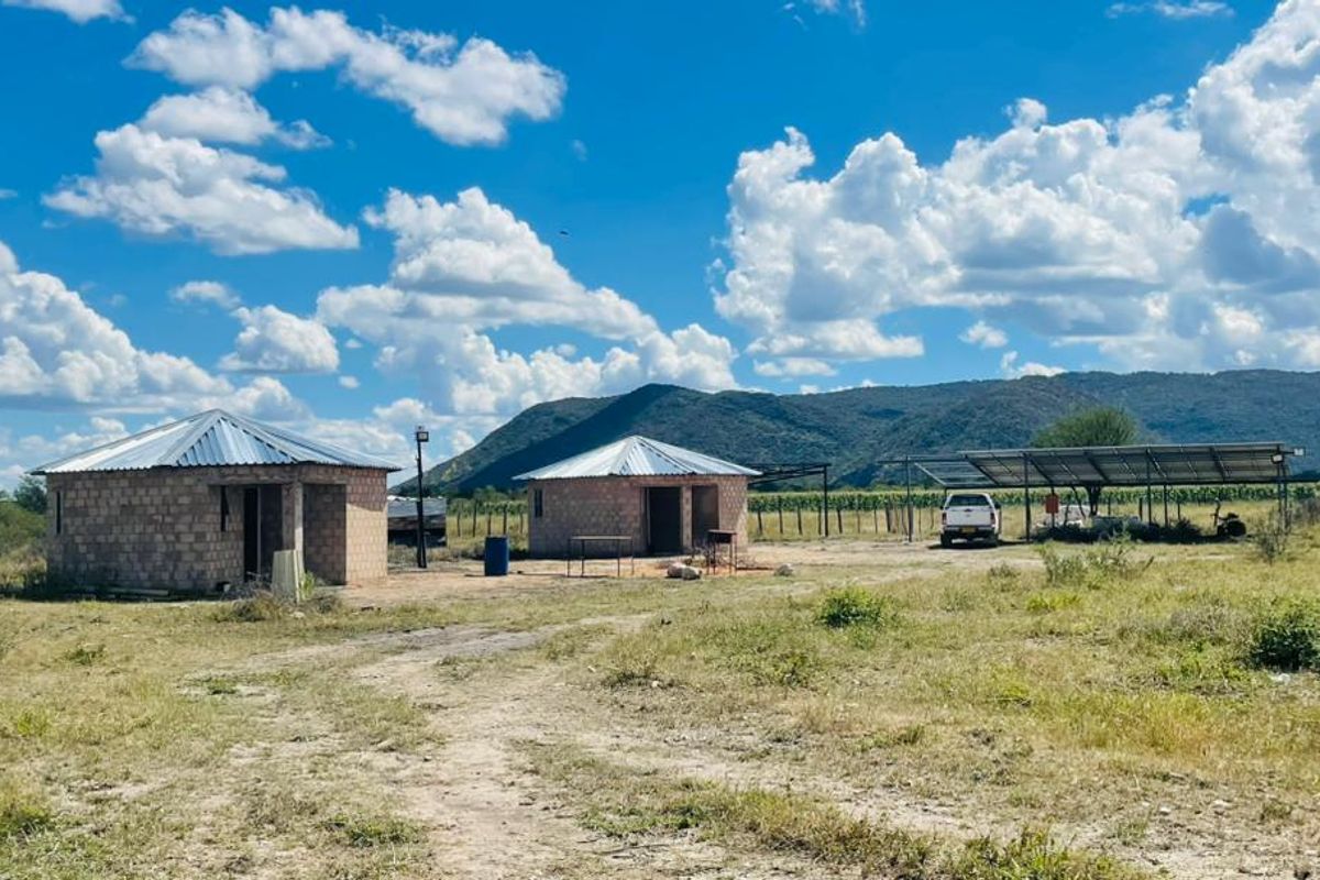 A rural farm property featuring two detached brick structures with metal roofs and a large solar panel installation set against a mountain backdrop.