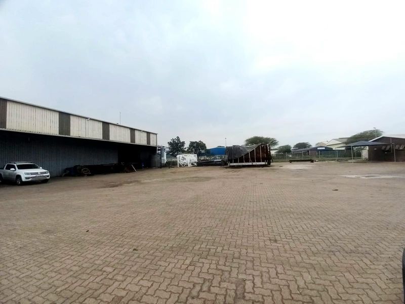 Spacious industrial yard featuring paved ground and a large warehouse structure with metal cladding.