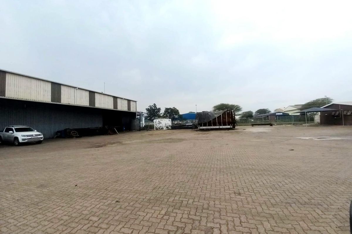 Spacious industrial yard featuring paved ground and a large warehouse structure with metal cladding.