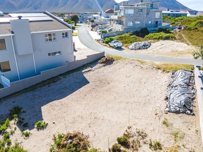 An aerial view of a vacant residential plot situated in a developed coastal neighborhood with surrounding boundary walls.