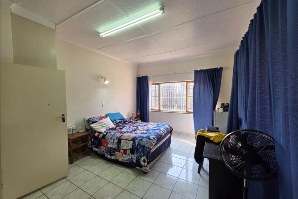 A functional bedroom featuring tiled flooring, a large window with security bars, and built-in storage space.
