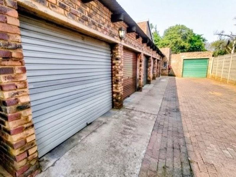 A row of garages featuring brick construction, roller shutter doors, and a paved driveway area.