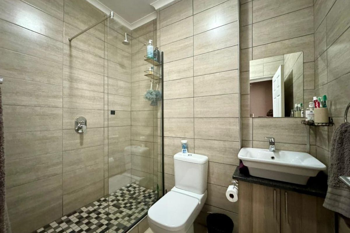Modern bathroom featuring a walk-in shower with glass screen, mosaic floor tiling, wall-mounted vanity with basin, and neutral wall tiles.