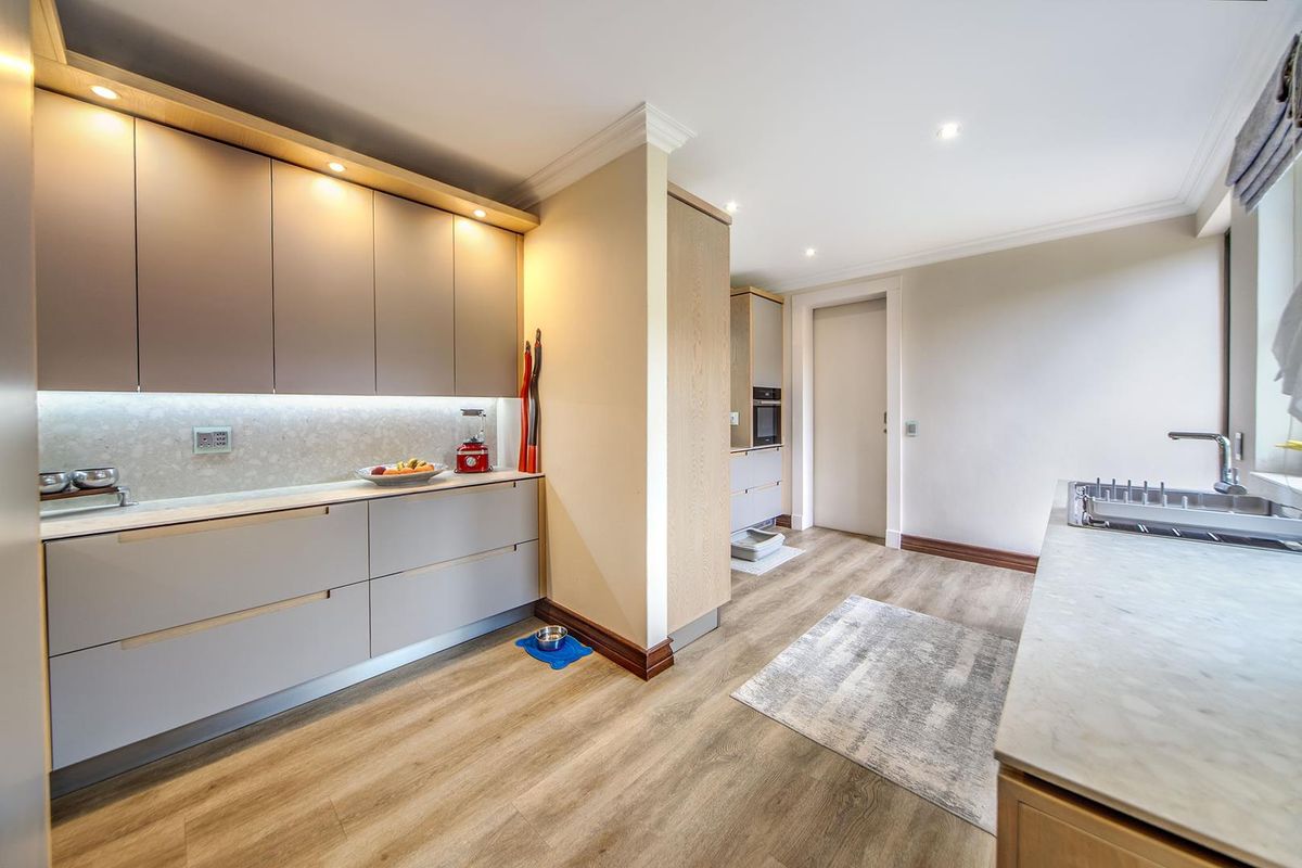 Modern kitchen featuring sleek handleless cabinetry, integrated lighting, stone-look countertops, and high-quality wood-look flooring in a clean, contemporary layout.