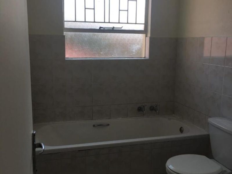 A functional bathroom featuring a built-in bathtub, toilet, and tiled finishes, complete with a window fitted with security bars.