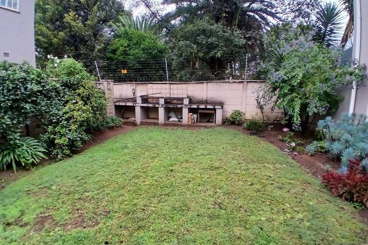 A private rear garden featuring a built-in masonry braai area, perimeter wall with electric fencing, and established garden beds.